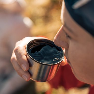 Nahaufnahme einer Person, die in der Natur ein Becher mit heißem Getränk hält und daraus trinkt, bei Sonnenlicht im Freien. | © Kleinwalsertal Tourismus eGen • Fotograf: Hannah Bichay