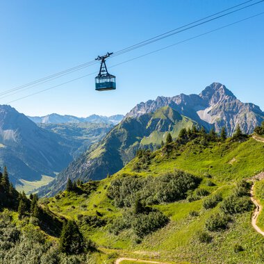 Bergbahn fährt über grüne Hänge und Berge im Kleinwalsertal, mit einem klaren blauen Himmel im Hintergrund. | © Oberstdorf · Kleinwalsertal Bergbahnen