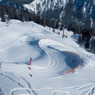 Snow-covered ski area with curves and avalanche barriers, surrounded by forest and mountains. | © Kleinwalsertal Tourismus eGen • Oberstdorf Kleinwalsertal Bergbahnen