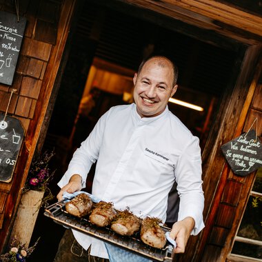 Man in chef's uniform holding a tray with grilled meat at a culinary festival in Kleinwalsertal. | © Kleinwalsertal Tourismus eGen • Fotograf: Sascha Gast